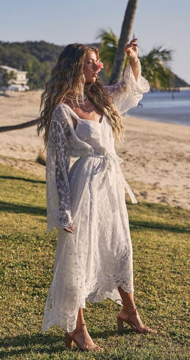 Woman in a white dress standing on a grassy area with a beach and palm trees in the background